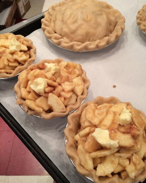 Three unbaked apple pies on a tray, with one large pie and two smaller ones filled with sliced apples and butter.