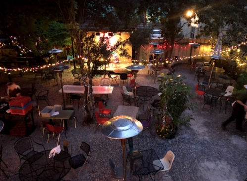 A cozy outdoor dining area with tables, chairs, and string lights, creating a warm, inviting atmosphere at night.