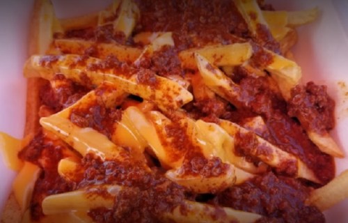 A close-up of fries topped with chili and melted cheese in a white container.