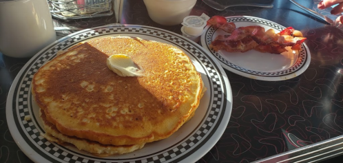 A stack of golden pancakes with butter on top, served with a side of crispy bacon.
