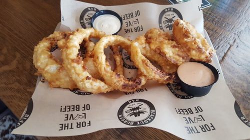 A plate of crispy onion rings served with two dipping sauces on a paper-lined table.