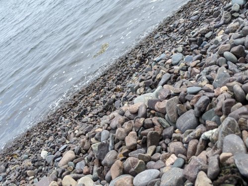 A rocky shoreline with smooth stones and gentle waves lapping at the water's edge.