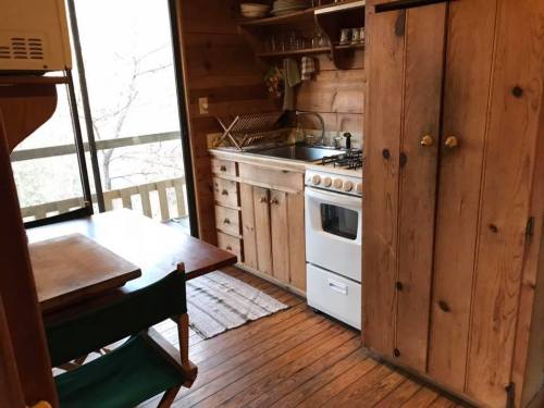 Cozy wooden kitchen with a stove, sink, and dining table, featuring rustic decor and natural light from a window.