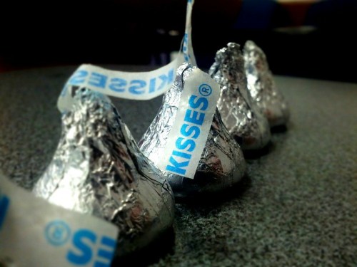 A close-up of several Hershey's Kisses chocolates wrapped in silver foil, lined up on a table.