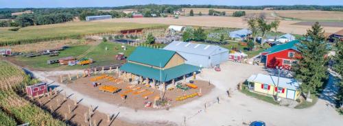 Aerial view of a farm with colorful buildings, pumpkin displays, and fields in the background on a sunny day.