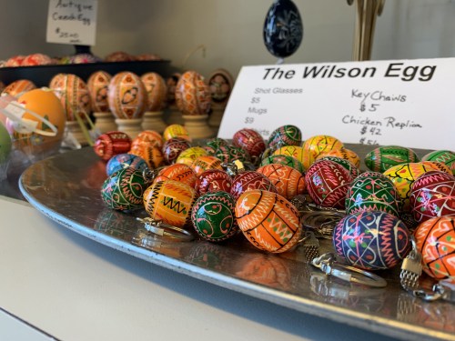 Colorful decorative eggs and keychains displayed on a tray, with a sign listing prices for various items.