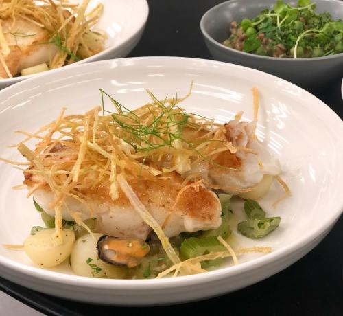 A plated dish featuring fish topped with crispy fried onions, served with vegetables and a side of greens.