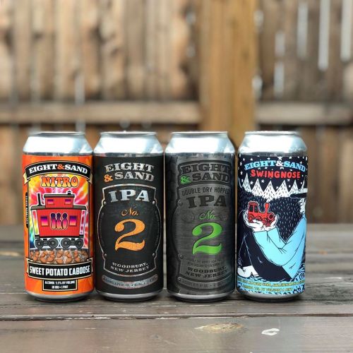 Four craft beer cans from Eight & Sand Brewing, featuring colorful designs and labels, arranged on a wooden table.