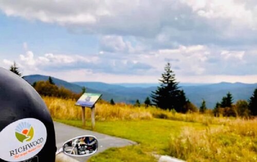A scenic view of mountains and trees, with a motorcycle helmet featuring a "Richwood" sticker in the foreground.