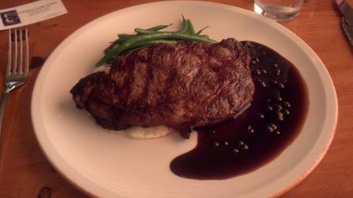 A plated steak with green beans and a dark sauce, served on a bed of mashed potatoes.