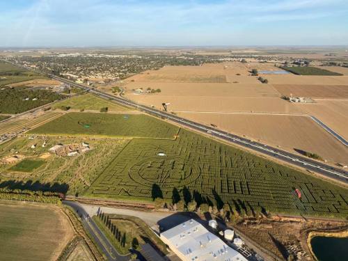 Aerial view of a large agricultural area with fields, a maze, and a highway running alongside.