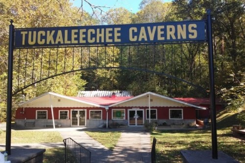 Sign for Tuckaleechee Caverns in front of a red and white building surrounded by trees and greenery.