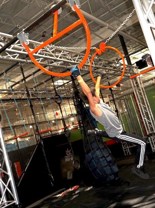 A person hangs from orange rings on a gym obstacle course, showcasing strength and agility.