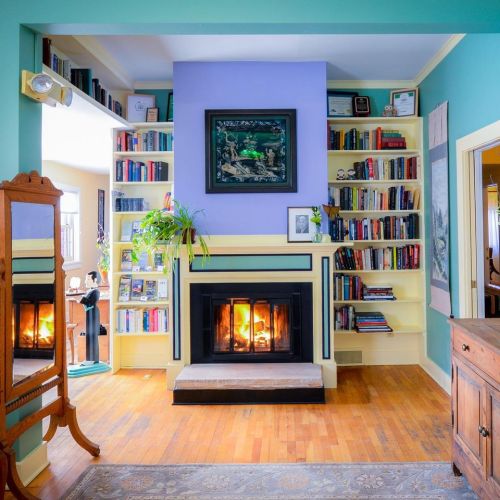 Cozy living room with a fireplace, colorful walls, bookshelves, and a mirror reflecting warm light.