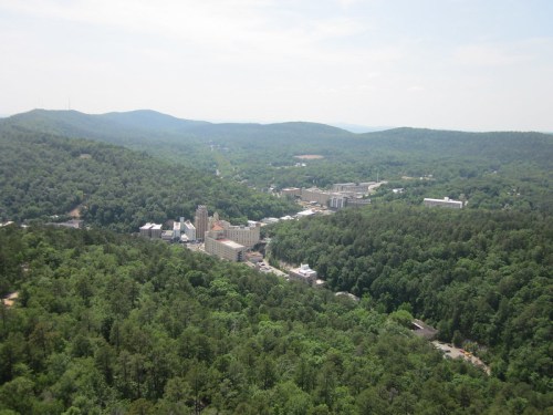Aerial view of a lush green landscape with a small town nestled among the hills and trees under a clear sky.
