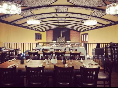 Elegant restaurant interior with wooden tables, chairs, and a decorative ceiling, featuring chandeliers and a spacious layout.