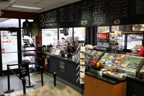 Interior of a café with a counter displaying menu items, coffee, and a seating area visible through large windows.