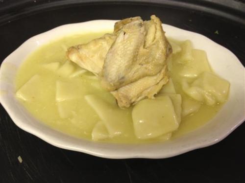 A plate of chicken and dumplings in a creamy broth, featuring a whole chicken piece on top of the dumplings.