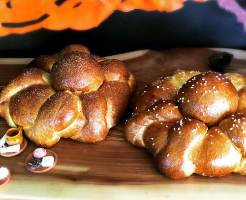 Two beautifully braided loaves of bread, one topped with sesame seeds, displayed on a wooden board.