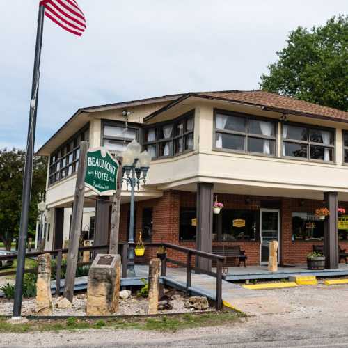 A two-story hotel with a porch, surrounded by greenery, and an American flag waving in the background.