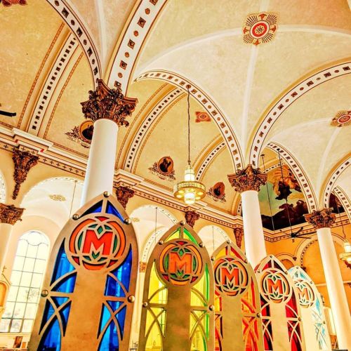 Colorful stained glass panels in a grand architectural interior with ornate ceilings and decorative details.
