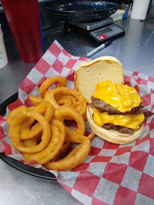 A plate with a cheeseburger topped with melted cheese and bacon, accompanied by a side of crispy onion rings.