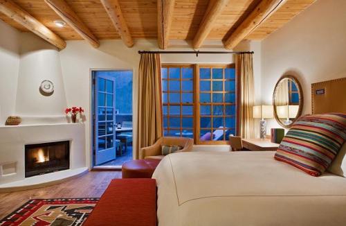Cozy bedroom with wooden beams, a fireplace, and a view of a patio through large windows. Warm, inviting decor.
