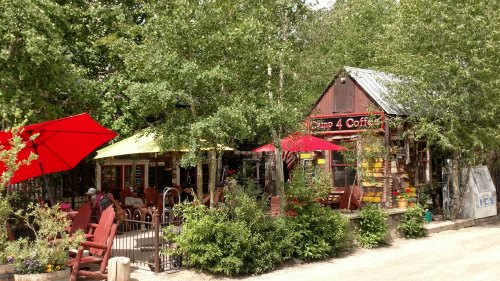 A cozy coffee shop with colorful umbrellas, surrounded by greenery and outdoor seating.