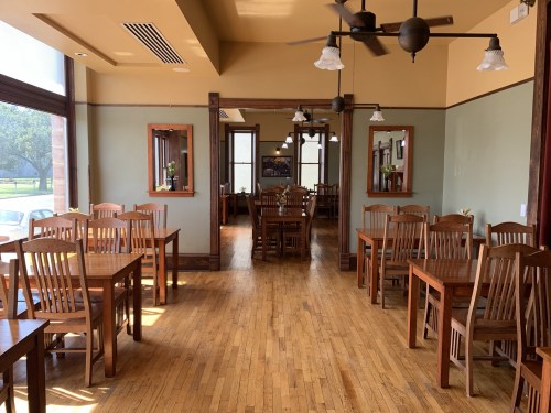 A spacious restaurant interior with wooden tables and chairs, large windows, and a warm color scheme.