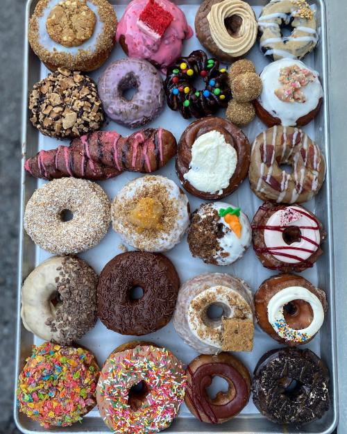 A tray of assorted donuts in various flavors and toppings, including sprinkles, chocolate, and fruit.