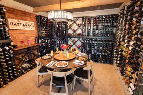 A cozy dining area with a round table set for a meal, surrounded by a wall of wine bottles and a warm ambiance.