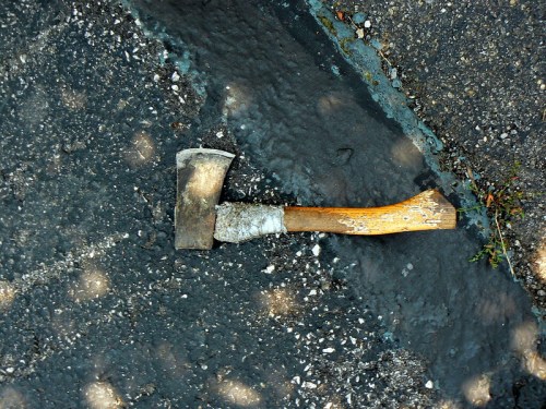 An old axe with a wooden handle lying on a cracked, dark surface.