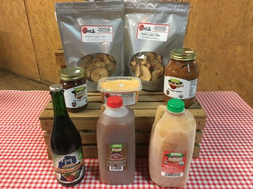 A display of various organic food products, including apple chips, cider, and preserves, arranged on wooden crates.