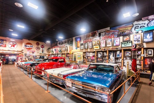 A vintage car museum featuring classic cars, memorabilia, and Route 66 signs displayed along the walls.