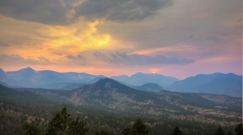A scenic view of mountains at sunset, with a colorful sky and soft clouds illuminating the landscape.