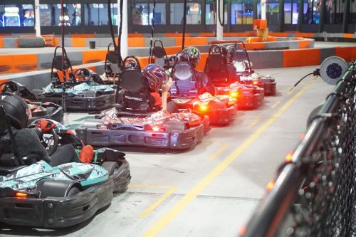 A row of go-karts lined up on a track, with drivers wearing helmets and colorful lights illuminating the scene.