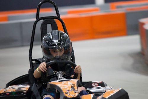 A child in a helmet drives a go-kart on a racetrack, focused and determined.