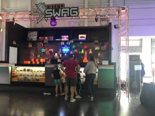 A colorful booth with a sign reading "Nitto Swag," featuring kids and adults interacting with various items.