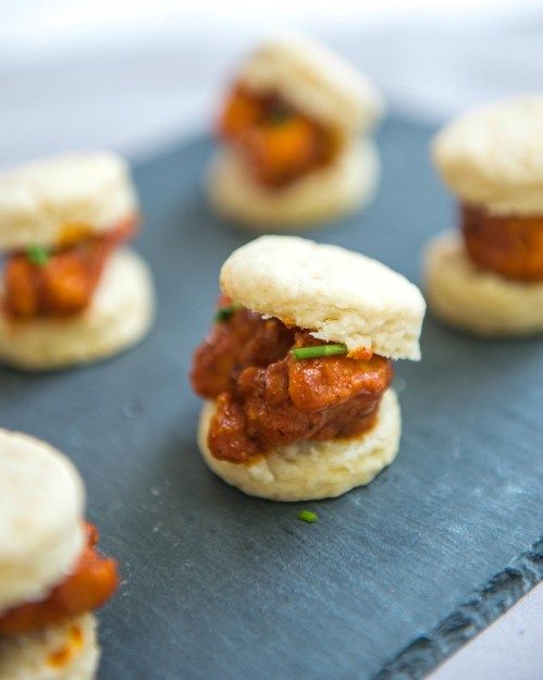 Mini biscuits filled with savory chicken, garnished with chives, served on a slate platter.