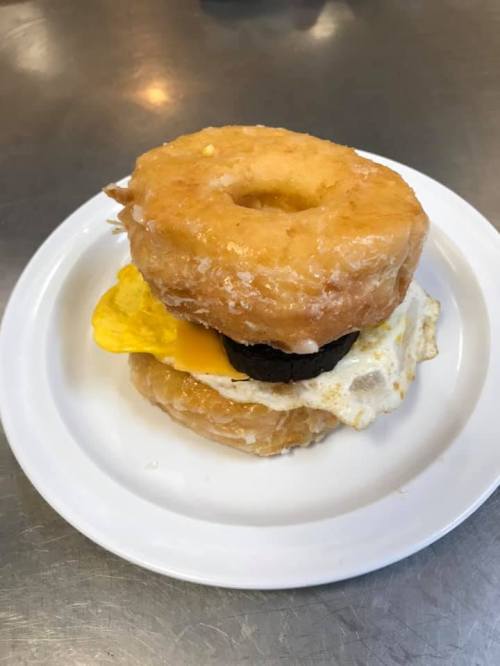A glazed donut sandwich with a fried egg and cheese in between two donut halves on a white plate.