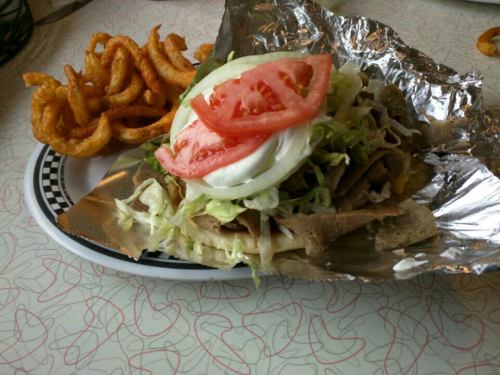 A plate with a foil-wrapped taco topped with lettuce, tomato, and a dollop of sour cream, alongside curly fries.