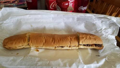 A long sandwich cut into sections, resting on white paper, with drinks and condiments in the background.