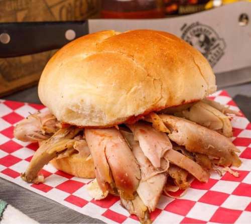 A hearty sandwich filled with tender, shredded meat on a soft bun, served on a red and white checkered paper.