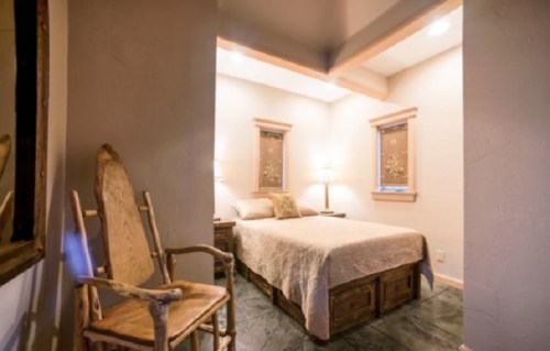 Cozy bedroom with a bed, wooden furniture, and soft lighting, featuring a rustic chair and decorative windows.