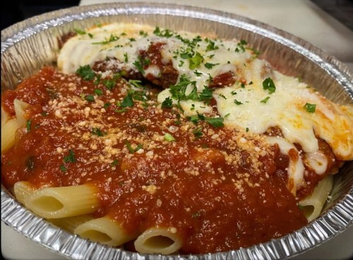A foil container filled with pasta, marinara sauce, and cheese, garnished with parsley.