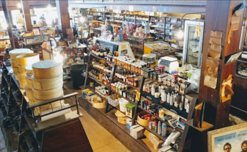 A vintage store interior filled with shelves of various products, including jars, bottles, and wooden barrels.