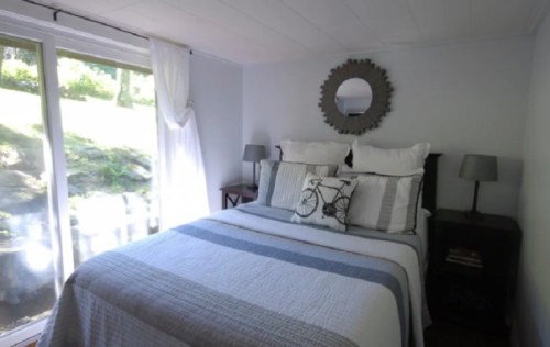 Cozy bedroom with a bed, decorative pillows, a mirror, and natural light from a window.