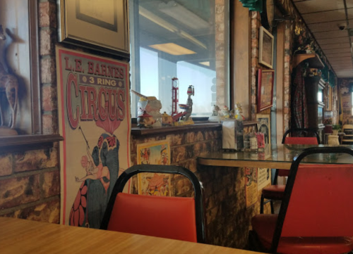A cozy diner interior with vintage circus posters, brick walls, and empty tables and chairs.