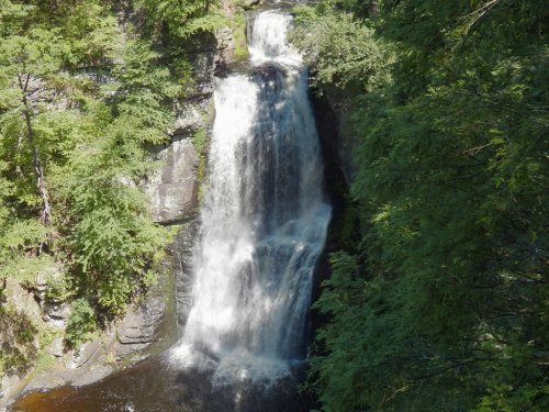 A cascading waterfall surrounded by lush green trees and rocky cliffs, creating a serene natural scene.