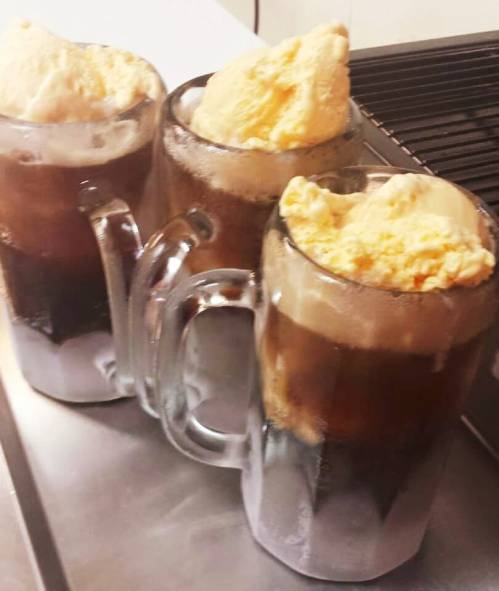 Three frosty mugs filled with root beer and topped with scoops of vanilla ice cream.